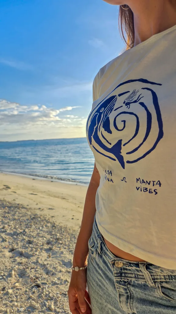 Remera blanca de Alma Curva y Manta Vibes con la ballena, puesta en la playa