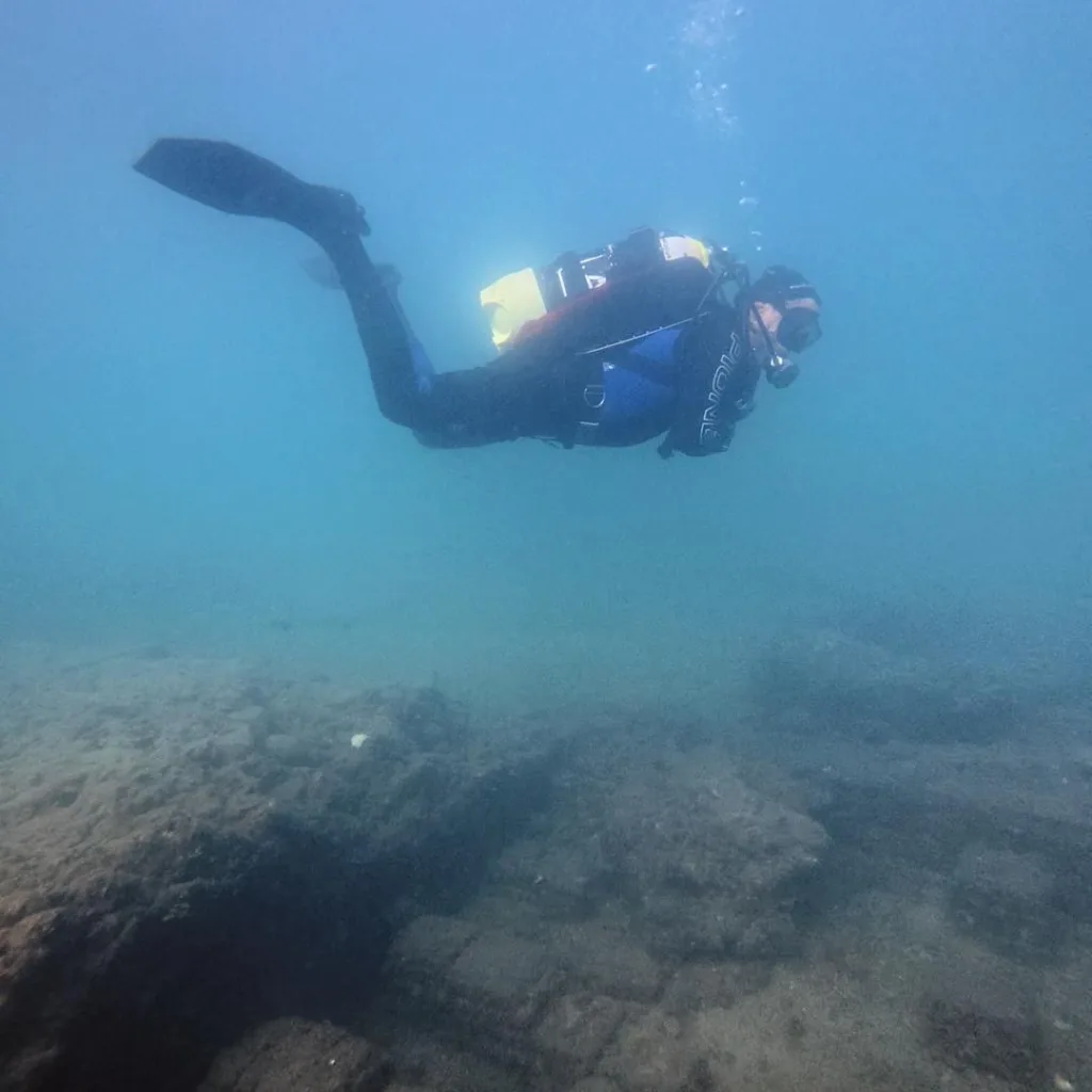 Buzo nadando sobre ruinas romanas de ladrillo en el fondo del mar, en Baia
