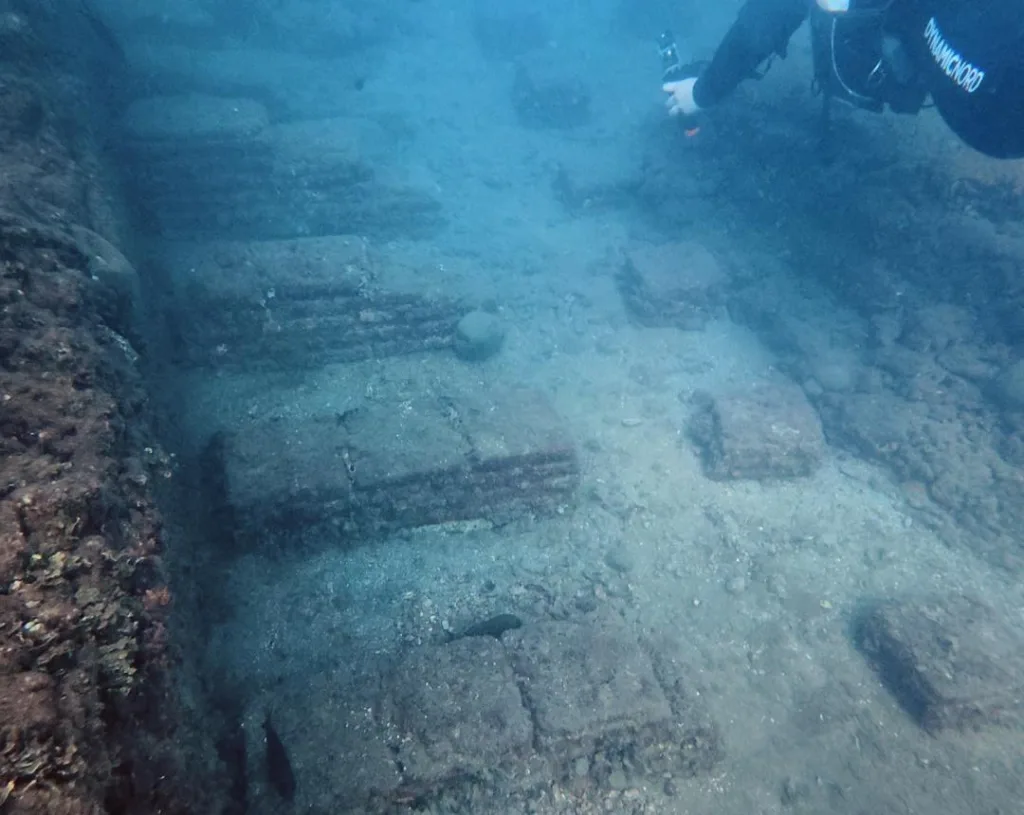 Buzo recorriendo hileras de pilares de ladrillo romanos bajo el agua en Baia