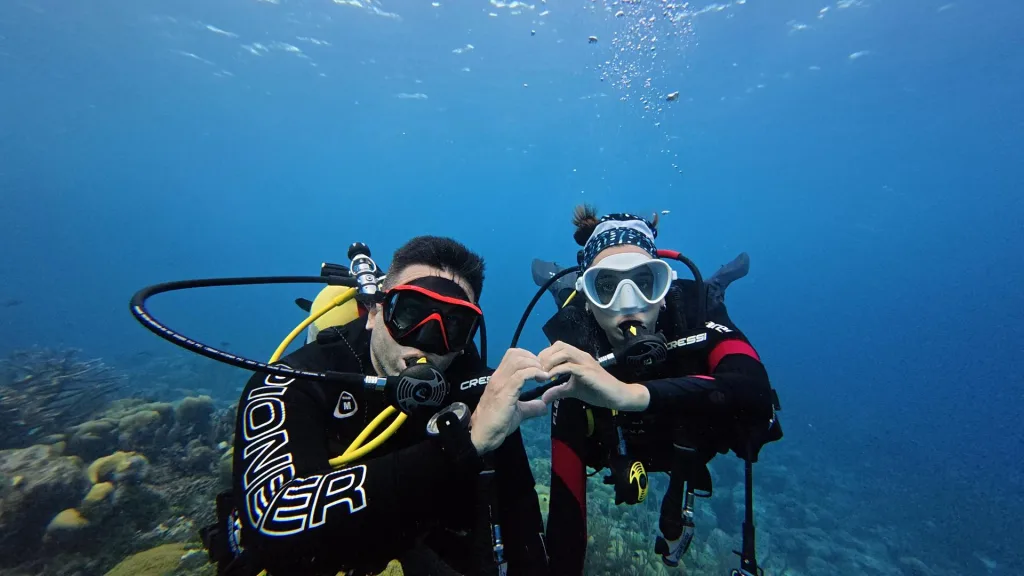 Mile y Joe haciendo un corazón con las manos bajo el agua, sobre el arrecife