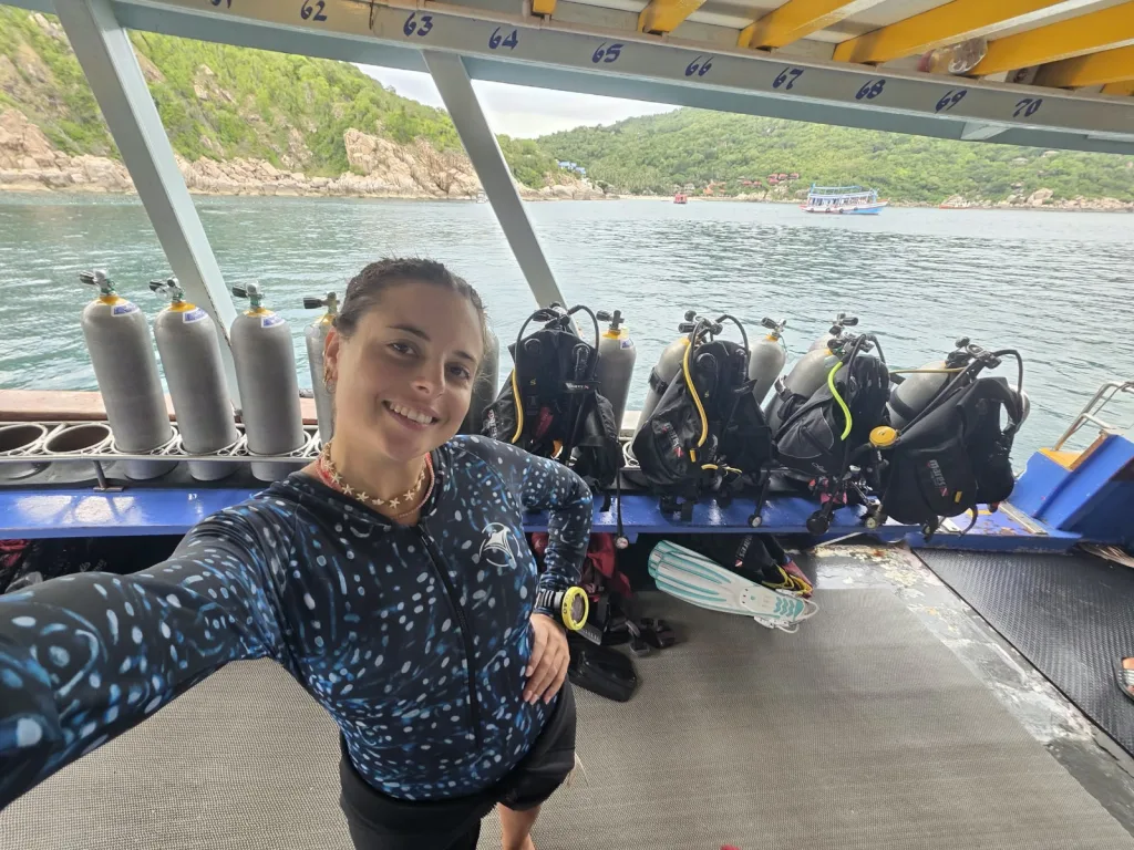 Dalina sonriendo en un barco de buceo, con una remera de Manta Vibes y los equipos detrás