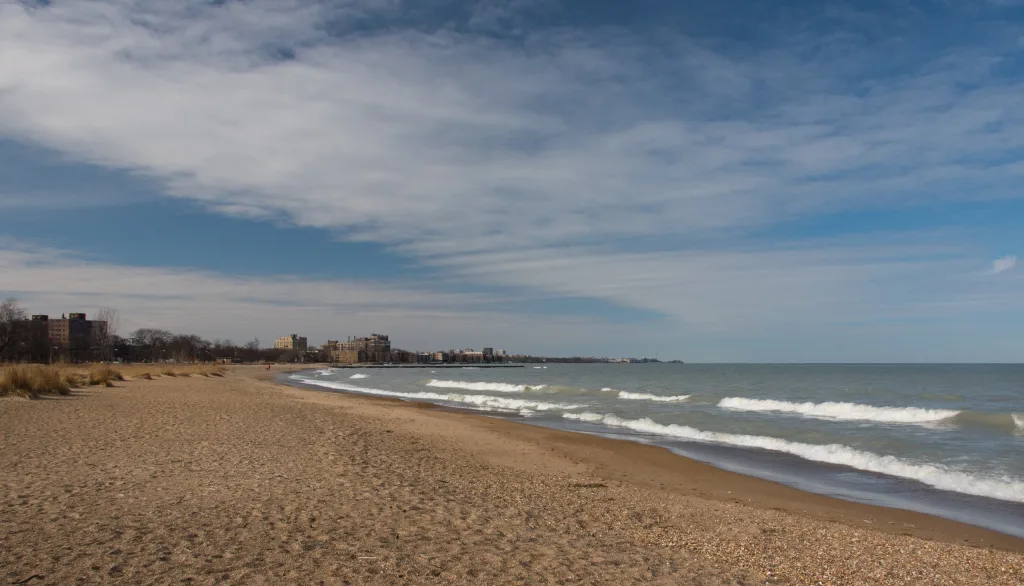 Playa de arena con olas suaves bajo un cielo azul con nubes